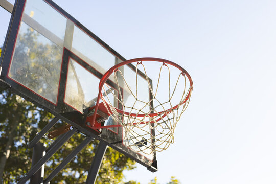 Plexiglass backboard and red rim with white braided net are glinting in sunlight at park