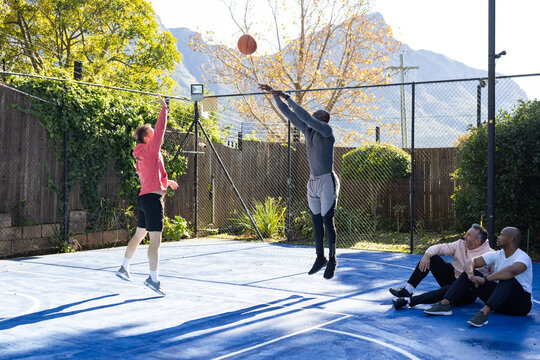 Four men playing basketball on backyard blue court, jumping and blocking in shorts with midair ball