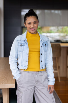 African woman standing beside wooden table in home kitchen, wearing denim jacket, cargo pants