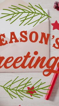 Animation of seasons greetings over envelope, stars, sticks, gift box, cherries and bauble on table