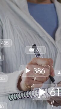 Animation of social media icons floating against caucasian senior woman taking notes at home