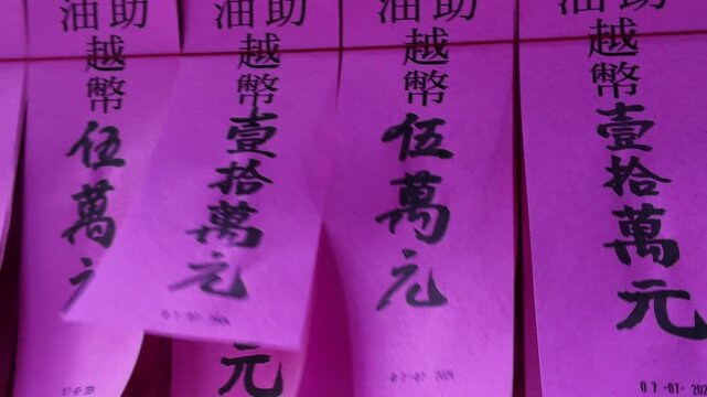 Close-up view of traditional pink donation slips and prayer blessings with Chinese calligraphy pasted on walls inside a historic Chinese temple in Cholon, District 5, Ho Chi Minh City, Vietnam.