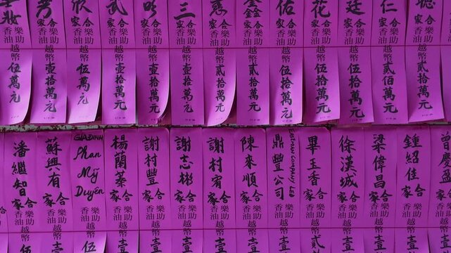 Close-up view of traditional pink donation slips and prayer blessings with Chinese calligraphy pasted on walls inside a historic Chinese temple in Cholon, District 5, Ho Chi Minh City, Vietnam.