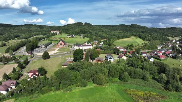 Aerial mountain valley Blizne Poland village pull 2. South eastern Poland. Historic mountain valley village with 15th century wooden All Saints Church. Agriculture land, rivers, forest and rural farm.
