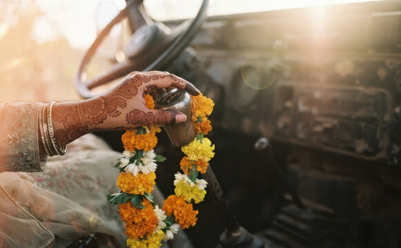 Traditional Indian bride hand with henna tattoo holding a flower garland on a car gear shift