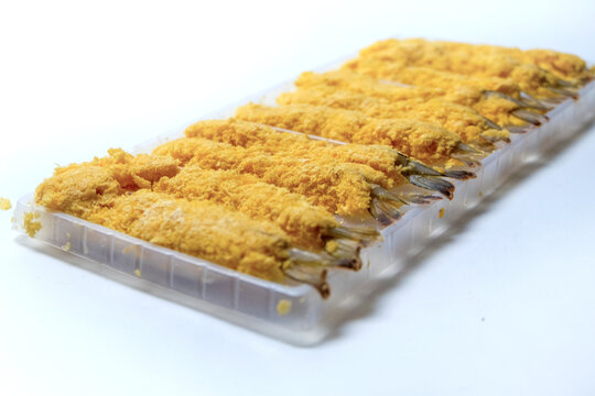 Side-angle shot of raw breaded Ebi Furai arranged neatly in a plastic tray against a clean white background.