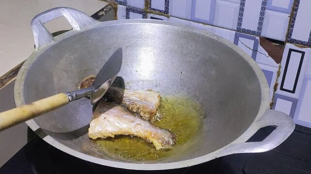 Flipping frying fish using a spatula in a hot pan at home kitchen