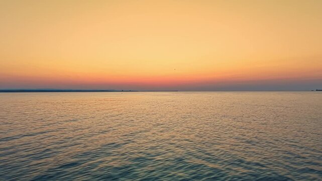 A view of the ocean at sunset shows gentle waves and a soft gradient of colors in the sky. The horizon is far in the distance with no land in sight.