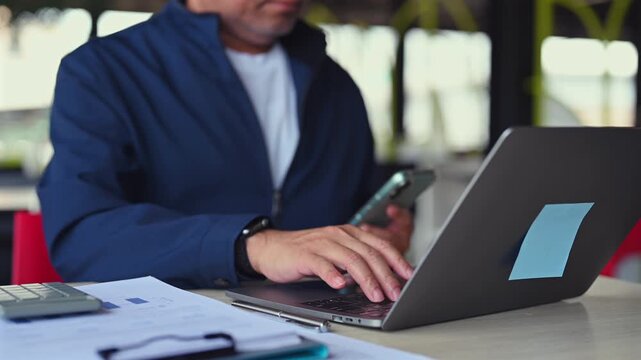 Focused professional manages business work seated desk side, completing daily work duties regarding corporate business, conducting digital work over laptop computer.