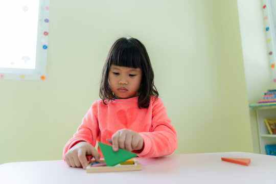 Focused young child concentration playing with wooden tangram puzzle on table in playroom.