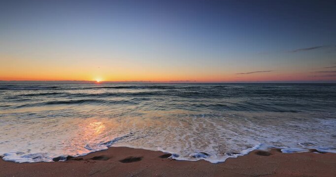 Peaceful Sunset Over Ocean Waves With Sandy Beach, Gentle Shoreline, and Footprints