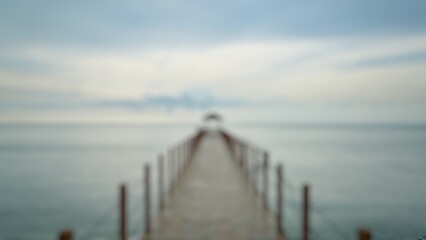 Obraz premium Soft focus photograph of a wooden pier extending toward a calm sea under a cloudy sky, creating a peaceful and atmospheric coastal scene with a dreamy blurred effect.