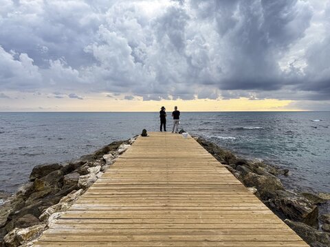 Two people standing on a jetty looking at the sea under a cloudy sky, Side, Manavgat, Antalya Province, Turkey