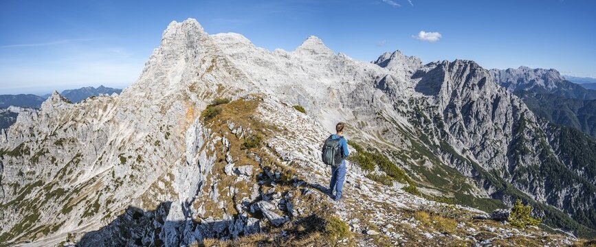 Hiker at the summit of Seehorn, hiking trail along a ridge, view of mountain landscape, in the background mountain ridge with peaks Schaflegg and Mitterhorn, Nuaracher H&ouml;henweg, Loferer Steinberge, Tyrol, Austria