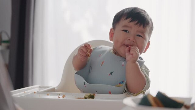 Asian Baby Using Finger to Feed Herself a Food with Baby Led Weaning Concept.Cute Asian baby boy eating finger food in high chair.