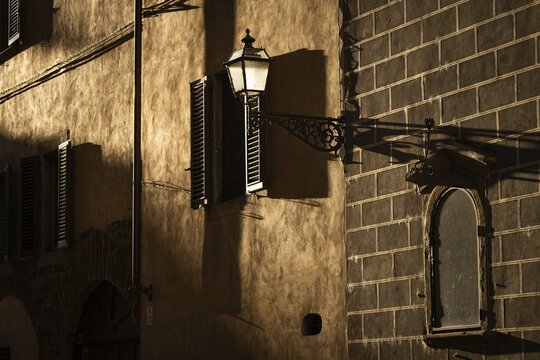 A house wall illuminated by evening sun with windows and a street lamp that casts shadows, old town, Florence, Tuscany, Italy