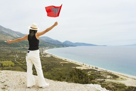 Elegant woman on viewpoint holding Albanian flag above Albanian Riviera coastline mountain national celebration freedom patriotism Vlore Albania