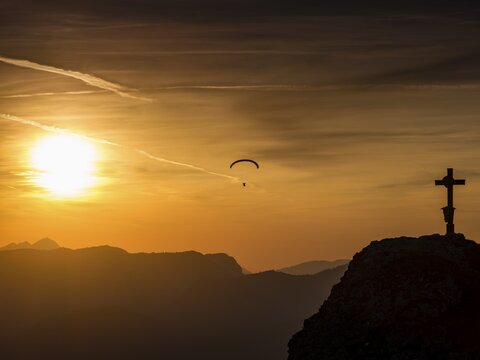 Paraglider flying next to the summit cross of the small Jenner at sunset, Reiteralpe in the background, Berchtesgaden National Park, Sch&ouml;nau am K&ouml;nigssee, Upper Bavaria, Bavaria, Germany