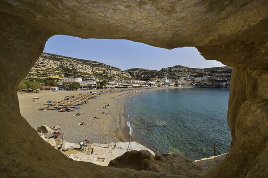 View through a rock opening onto a wide sandy beach with blue water, Matala, Neolithic caves, former hippie paradise, central south coast, Crete, Greek Islands, Greece