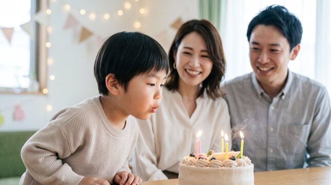 誕生日パーティーでケーキのろうそくを吹き消す男の子と見守る家族