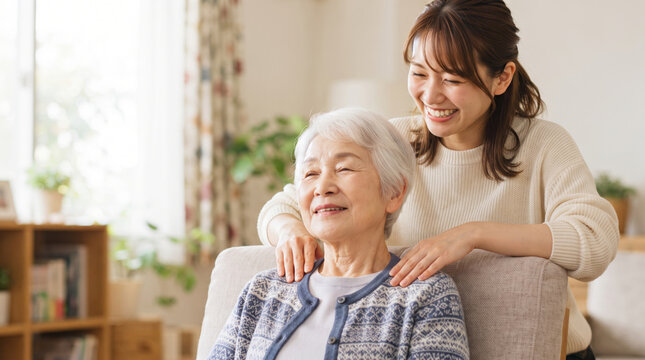 リビングで高齢女性の肩を揉んで介護ケアをする若い女性