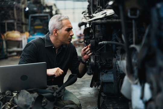 Supervisor with laptop inspecting used car engines in automotive spare parts warehouse