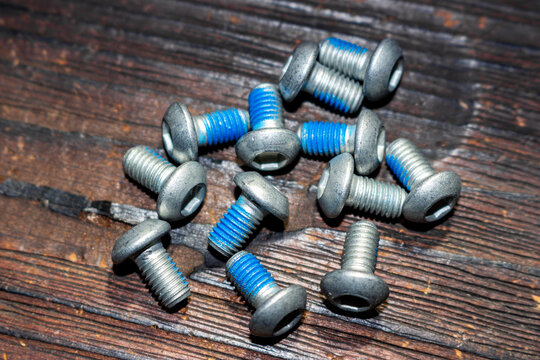 Steel hex bolts for bicycle disc brake rotors with applied blue threadlocker paste for secure assembly, arranged on a dark rustic wooden background for professional mechanical repair