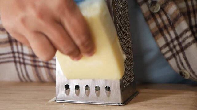 Woman hands grating hard cheese on metal grater in domestic kitchen