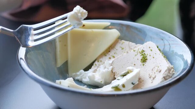 Close up cinematic shot of fresh cheese and Turkish halva on a plate, a fork is used to take a piece of the cheese to eat, motion footage