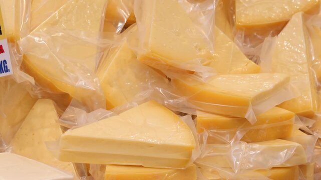 Close up motion footage of numerous vacuum-sealed cheese wedges displayed for sale, capturing their bright yellow color and clear packaging