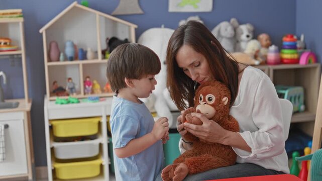 Woman holds a stuffed monkey while a little boy touches its hand and plays together in a playroom; tenderness bonding.