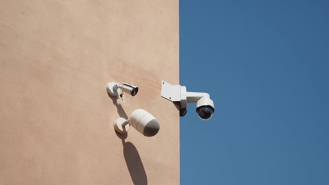 Multiple security cameras mounted on a wall with a bright blue sky in background