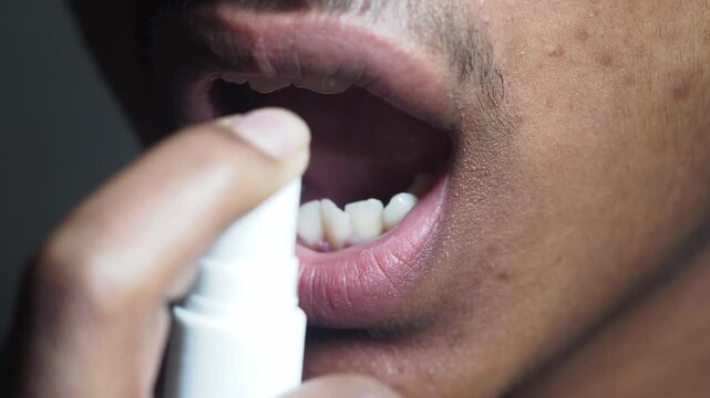 Close up shot of person spraying medicine into open mouth with teeth visible