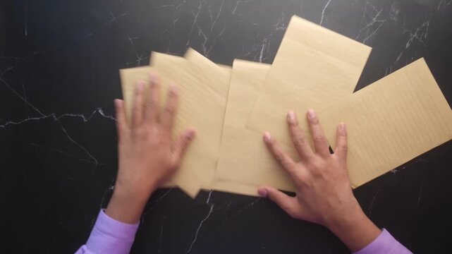 Hands spreading out yellow lined paper sheets on black marble surface in motion