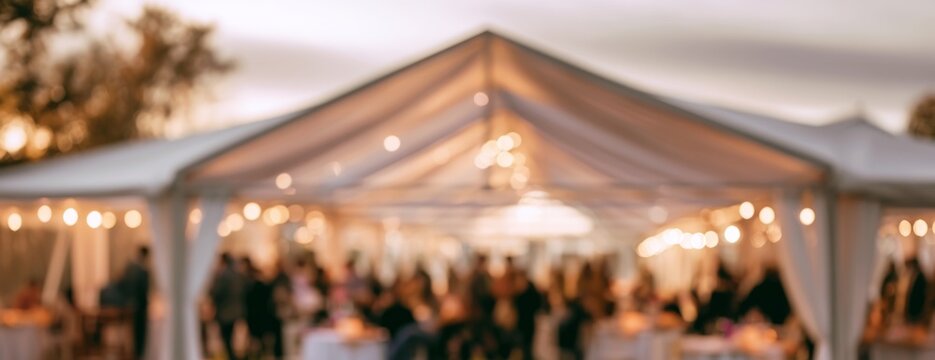 Outdoor event in a large white tent with guests celebrating, blurred background  
