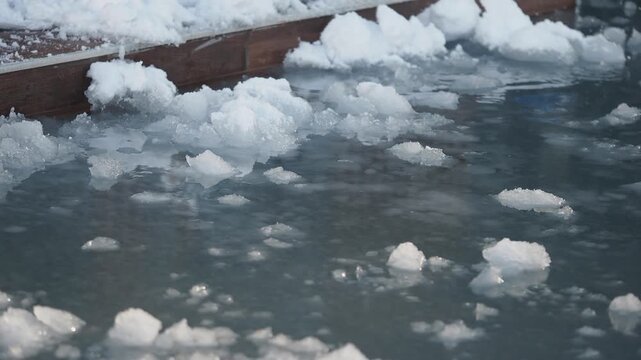 Floating ice chunks drift slowly on surface of murky water during cold weather