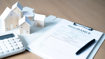 Obraz premium Wooden house models with insurance form, calculator and pen on desk, concept of home insurance, property protection, mortgage, financial planning, risk management and real estate investment.