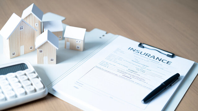 Wooden house models with insurance form, calculator and pen on desk, concept of home insurance, property protection, mortgage, financial planning, risk management and real estate investment.