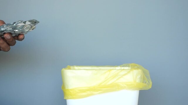 Person's hand discards empty medicine blister pack into trash bin with yellow liner footage