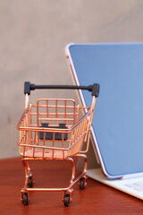 Miniature shopping cart in front of an open tablet with blank mockup screen on wooden table, online shopping and digital commerce concept. © Isman