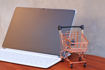 Miniature shopping cart in front of an open tablet with blank mockup screen on wooden table, online shopping and digital commerce concept. © Isman