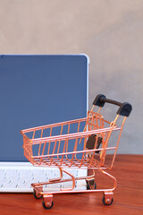 Miniature shopping cart in front of an open tablet with blank mockup screen on wooden table, online shopping and digital commerce concept. © Isman