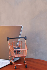 Miniature shopping cart in front of an open tablet with blank mockup screen on wooden table, online shopping and digital commerce concept. © Isman