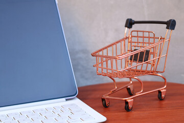 Miniature shopping cart next to a modern tablet with blank mockup screen on a wooden table, online shopping and e-commerce business concept with copy space. © Isman