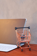 Miniature shopping cart in front of an open tablet with blank mockup screen on wooden table, online shopping and digital commerce concept. © Isman
