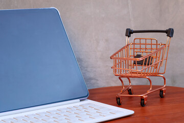 Miniature shopping cart next to a modern tablet with blank mockup screen on a wooden table, online shopping and e-commerce business concept with copy space. © Isman