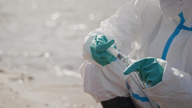 Ecologist in hazmat protective suit transferring water sample into test tube with syringe outdoors. Footage fits environmental crisis, pollution, and chemical safety projects