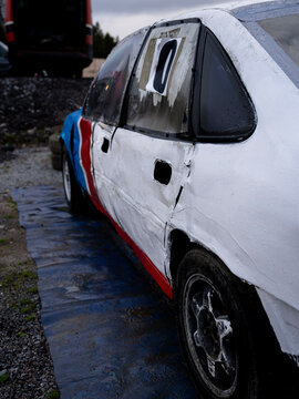 Close-up side view of a heavily worn and dented folkrace racing car with missing door handles, wet bodywork and visible damage from motorsport use.