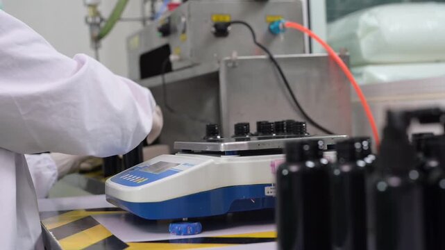 Laboratory scientist with glove handling black bottle filling production equipment, technology and sterile manufacturing process, laboratory equipment, quality control, precise measurement