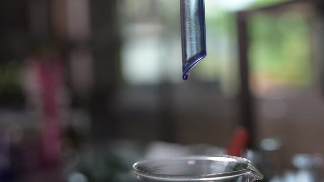 Laboratory glass pipette liquid drop beaker science experiment chemistry transparent equipment research blue liquid drop falling from glass pipette into clear beaker closeup create scientific